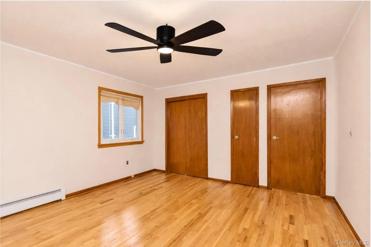 Unfurnished bedroom with multiple closets, a baseboard radiator, light wood-style floors, and ceiling fan Unfurnished bedroom with multiple closets, a baseboard radiator, light wood-style floors, and ceiling fan