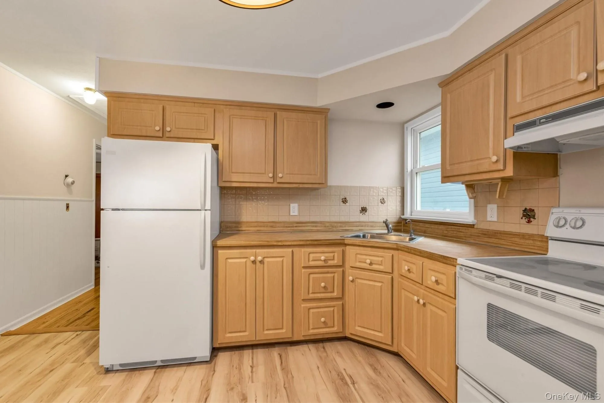 Kitchen with white appliances, light countertops, ornamental molding, light wood finished floors Kitchen with white appliances, light countertops, ornamental molding, light wood finished floors