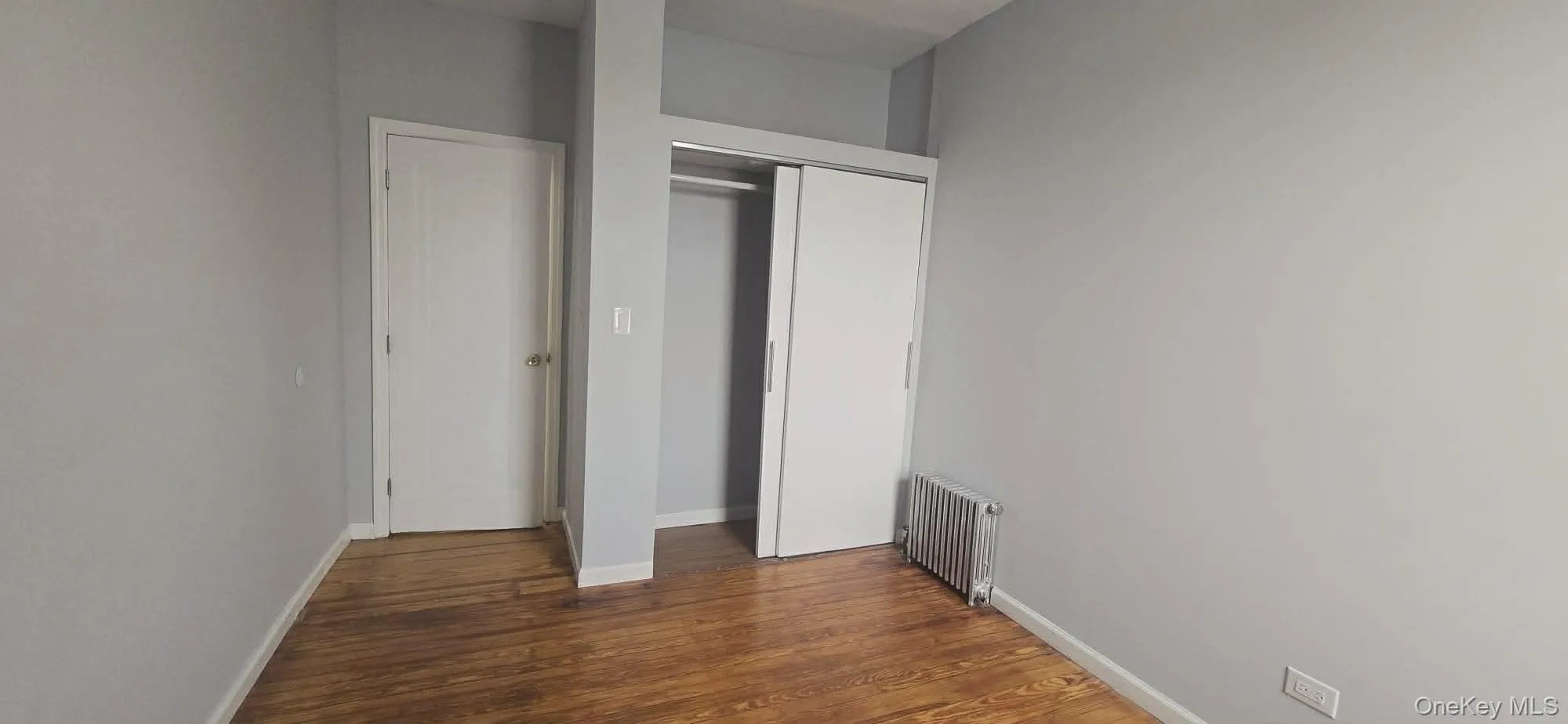 Unfurnished bedroom with radiator heating unit, a closet, and dark wood-style floors Unfurnished bedroom with radiator heating unit, a closet, and dark wood-style floors