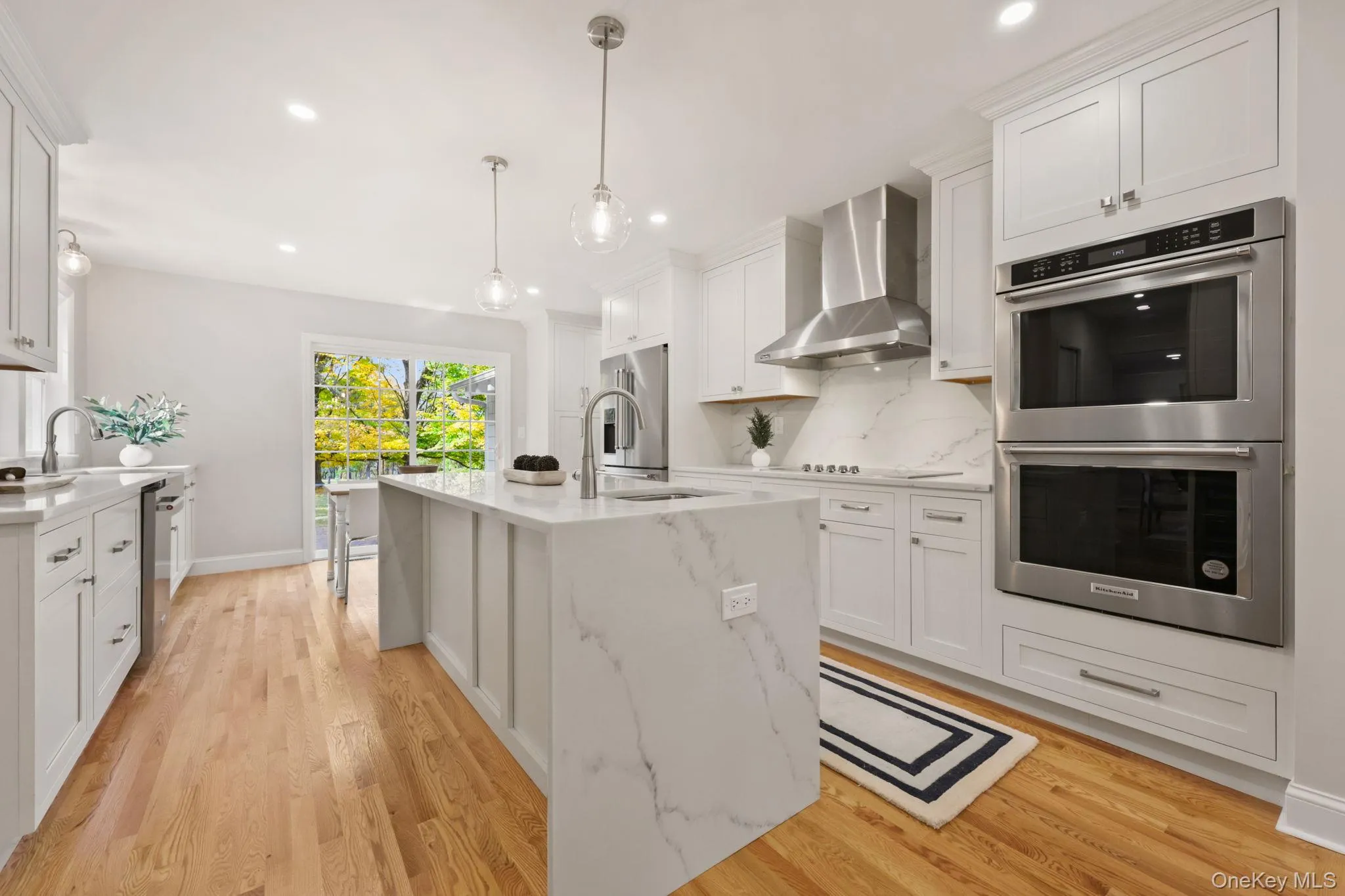 Kitchen with stainless steel appliances, light stone counters, wall chimney range hood, white cabinetry, and light wood finished floors Kitchen with stainless steel appliances, light stone counters, wall chimney range hood, white cabinetry, and light wood finished floors