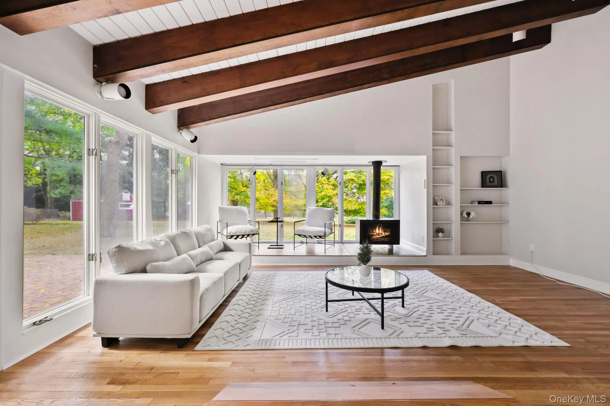 Living room featuring light wood finished floors, built in shelves, high vaulted ceiling, a lit fireplace, and a wood ceiling with exposed beams Living room featuring light wood finished floors, built in shelves, high vaulted ceiling, a lit fireplace, and a wood ceiling with exposed beams