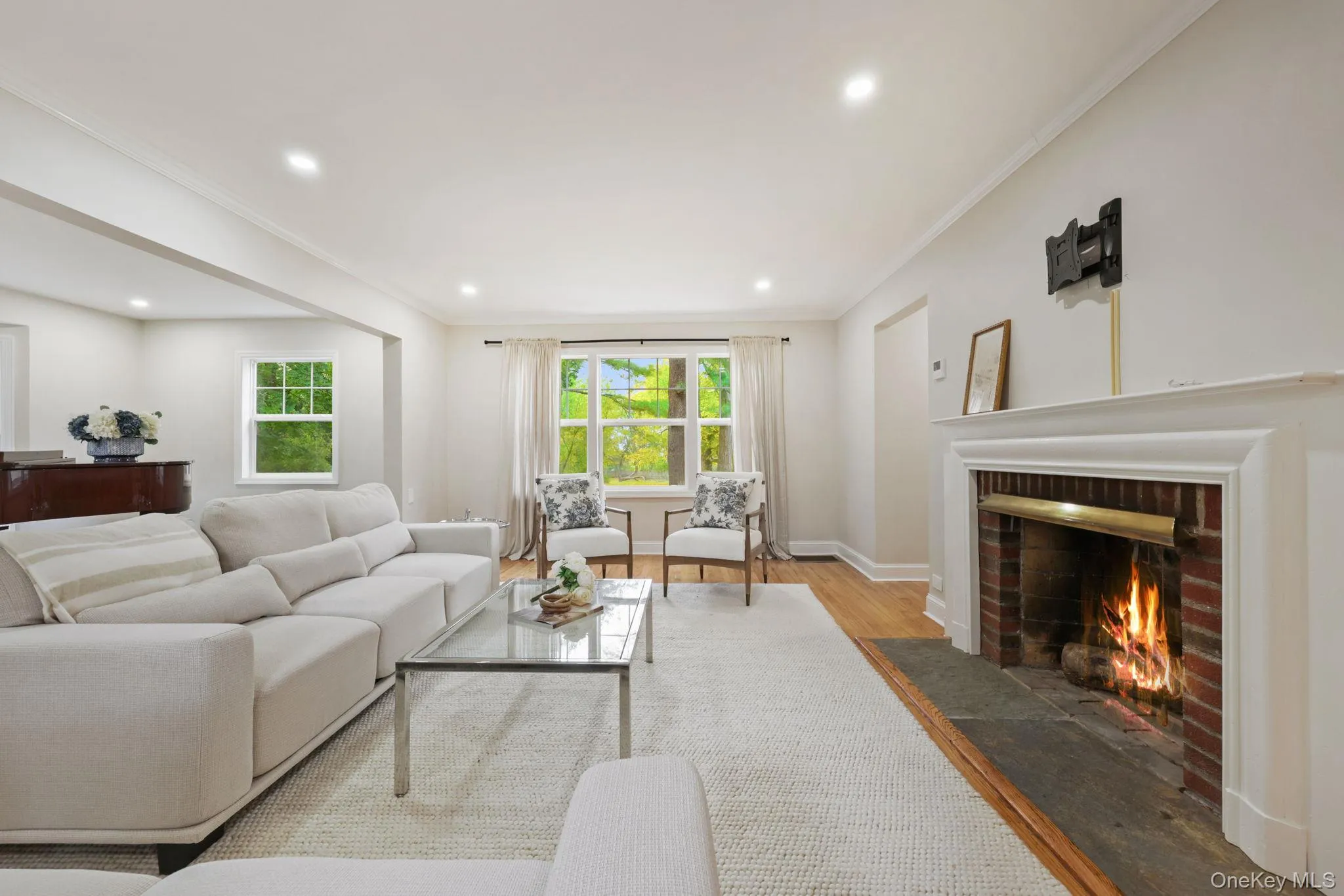 Living room featuring wood finished floors, crown molding, a brick fireplace, healthy amount of natural light, and recessed lighting Living room featuring wood finished floors, crown molding, a brick fireplace, healthy amount of natural light, and recessed lighting