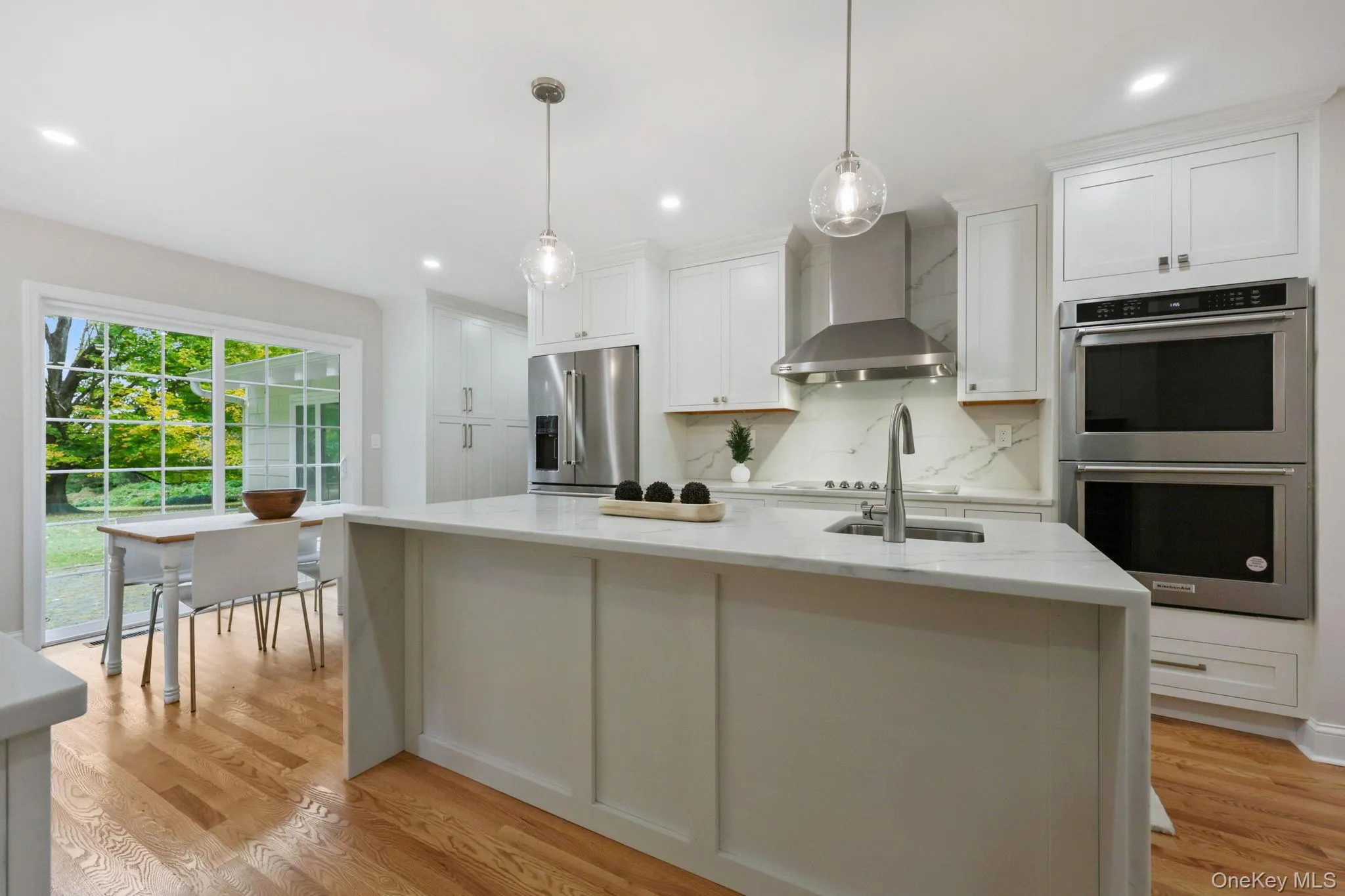 Kitchen with appliances with stainless steel finishes, light stone countertops, wall chimney range hood, white cabinetry, and decorative backsplash Kitchen with appliances with stainless steel finishes, light stone countertops, wall chimney range hood, white cabinetry, and decorative backsplash