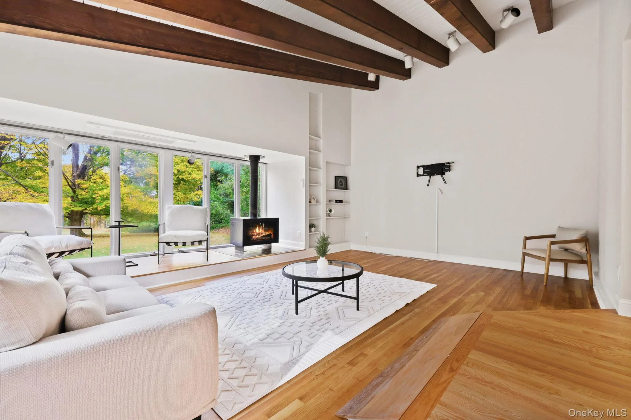 Living room with built in shelves, beamed ceiling, hardwood / wood-style floors, and a warm lit fireplace Living room with built in shelves, beamed ceiling, hardwood / wood-style floors, and a warm lit fireplace