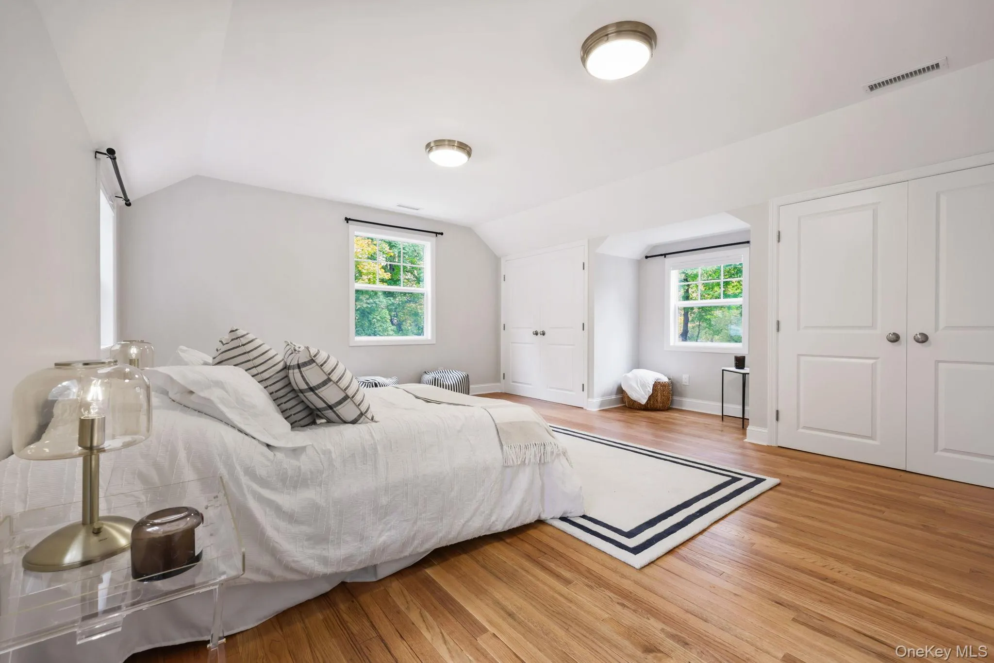 Bedroom featuring multiple windows, light wood-style floors, vaulted ceiling, and multiple closets Bedroom featuring multiple windows, light wood-style floors, vaulted ceiling, and multiple closets