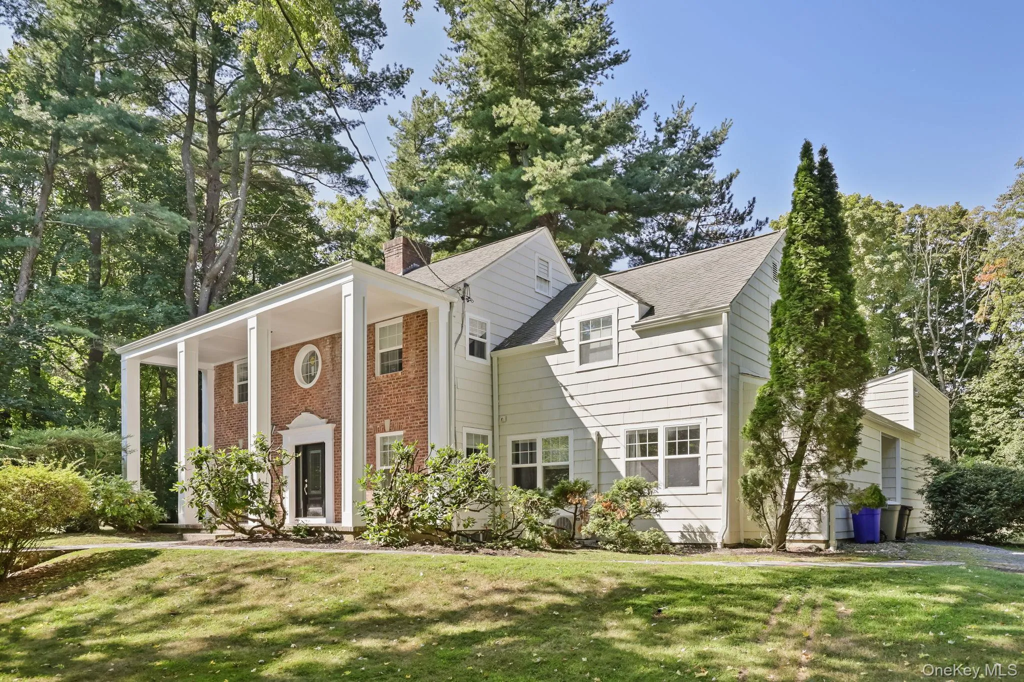 Neoclassical / greek revival house featuring a front lawn, covered porch, a chimney, and brick siding Neoclassical / greek revival house featuring a front lawn, covered porch, a chimney, and brick siding