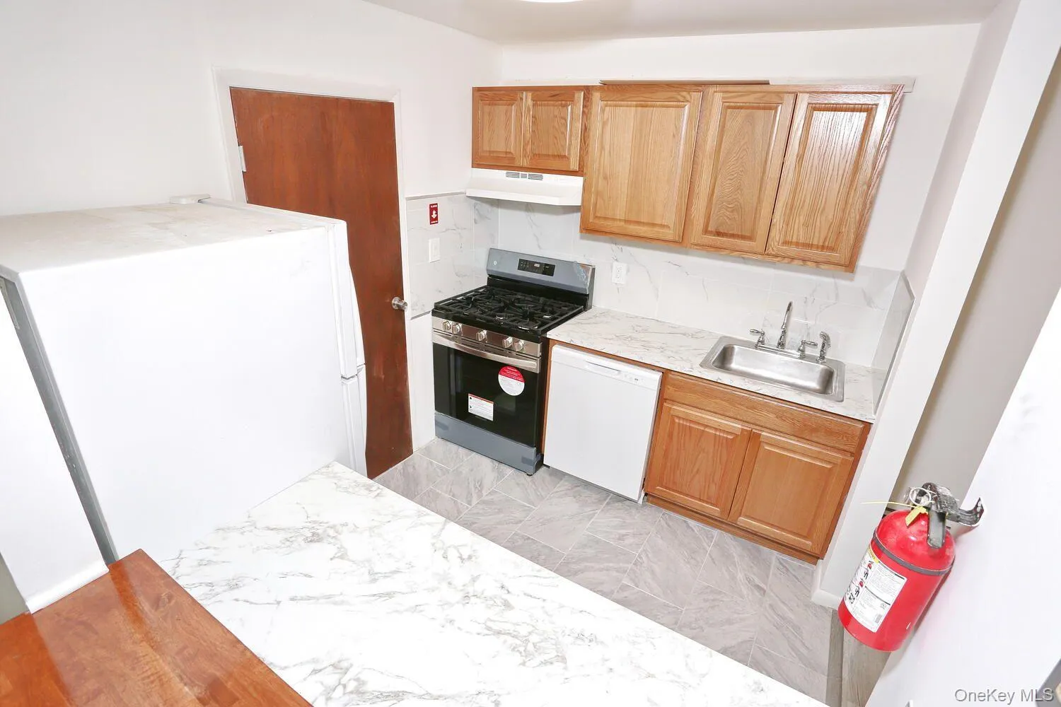 Kitchen with light marble finish flooring, white appliances, under cabinet range hood, tasteful backsplash, and brown cabinetry Kitchen with light marble finish flooring, white appliances, under cabinet range hood, tasteful backsplash, and brown cabinetry