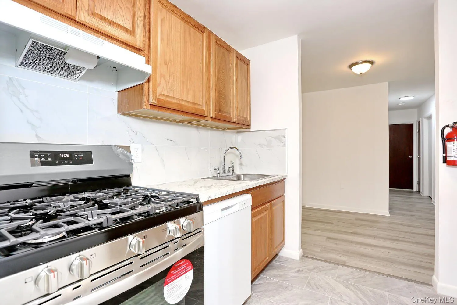 Kitchen with gas range, under cabinet range hood, white dishwasher, tasteful backsplash, and light stone counters Kitchen with gas range, under cabinet range hood, white dishwasher, tasteful backsplash, and light stone counters