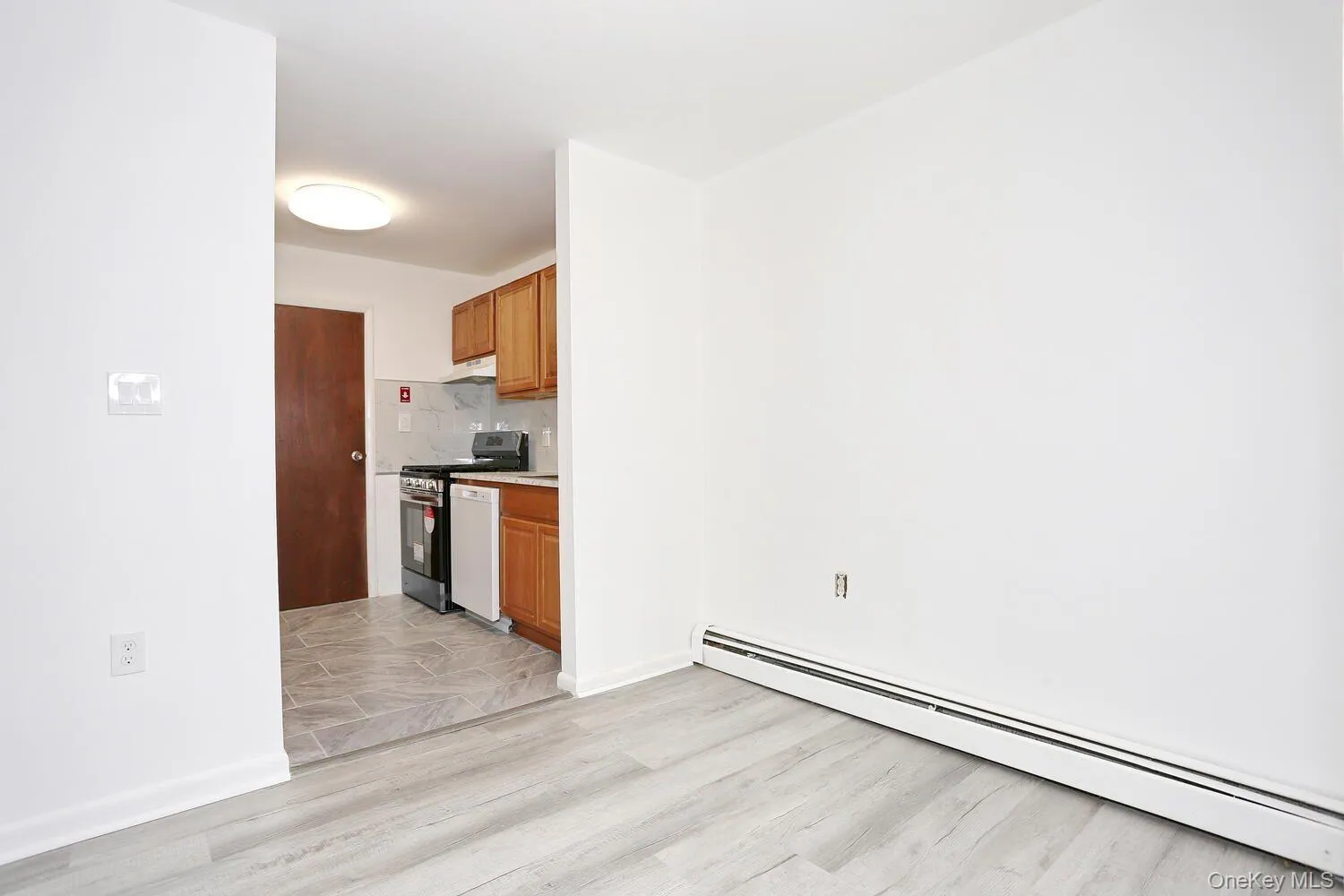 Kitchen featuring baseboard heating, stainless steel gas range oven, light countertops, brown cabinets, and white dishwasher Kitchen featuring baseboard heating, stainless steel gas range oven, light countertops, brown cabinets, and white dishwasher