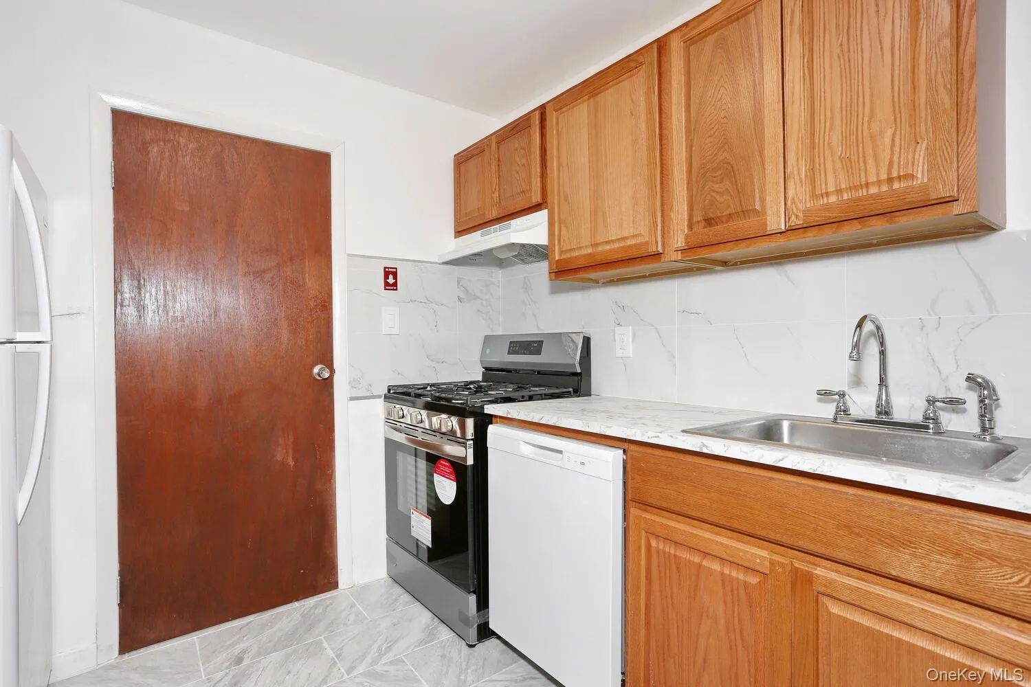 Kitchen featuring white appliances, light countertops, under cabinet range hood, decorative backsplash, and brown cabinets Kitchen featuring white appliances, light countertops, under cabinet range hood, decorative backsplash, and brown cabinets