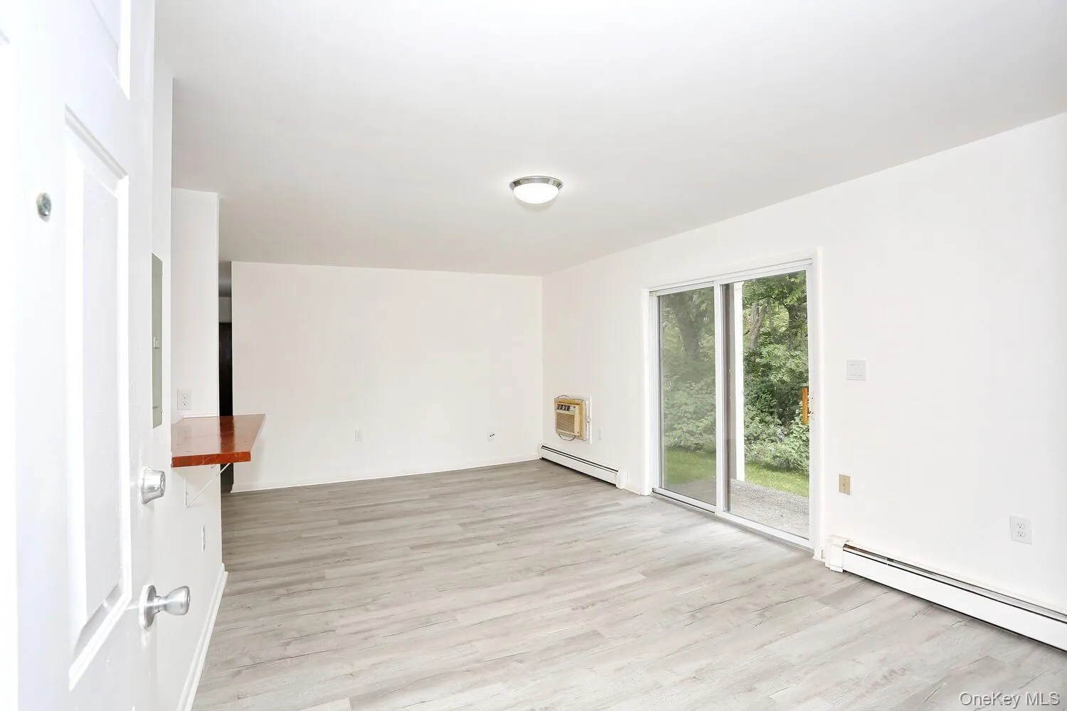 Empty room featuring a baseboard radiator, light wood-style flooring, and a wall mounted air conditioner Empty room featuring a baseboard radiator, light wood-style flooring, and a wall mounted air conditioner