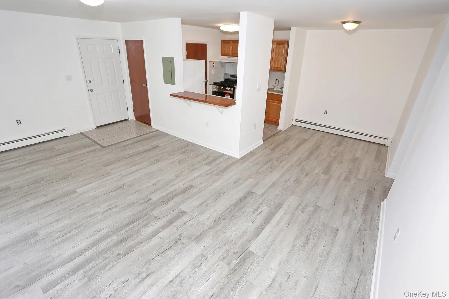 Kitchen with stainless steel gas range, a baseboard radiator, brown cabinetry, freestanding refrigerator, and light wood finished floors Kitchen with stainless steel gas range, a baseboard radiator, brown cabinetry, freestanding refrigerator, and light wood finished floors
