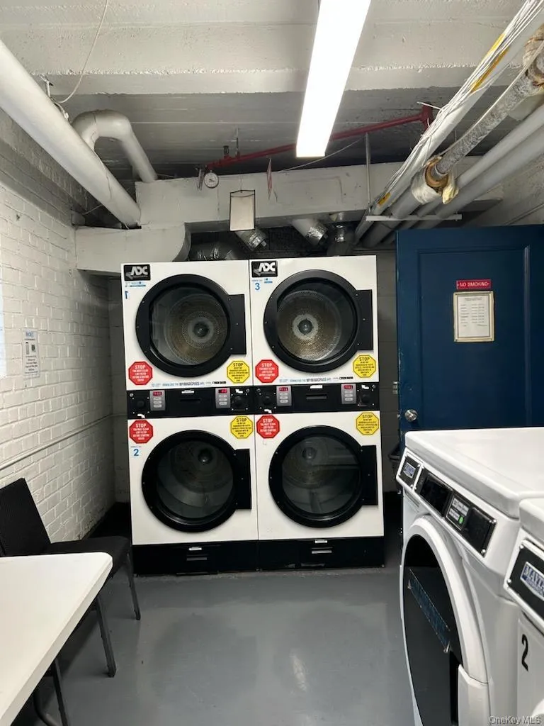 Shared laundry room featuring stacked washer / drying machine and brick wall Shared laundry room featuring stacked washer / drying machine and brick wall