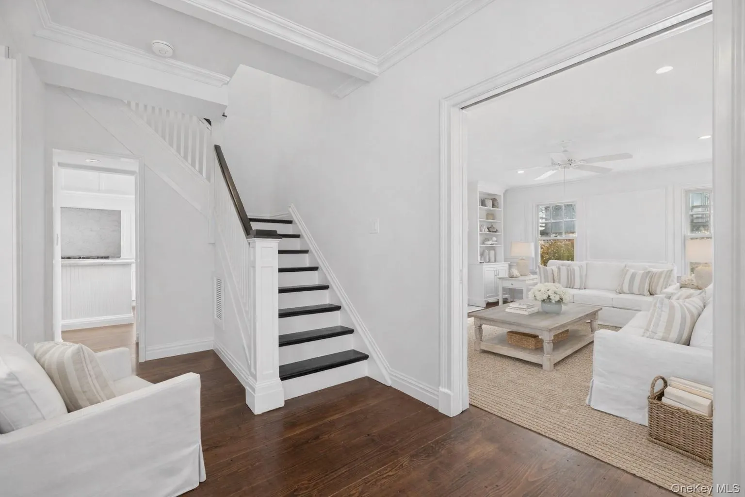 Living room with ornamental molding, dark wood-style flooring, built in shelves, stairs, and a ceiling fan Living room with ornamental molding, dark wood-style flooring, built in shelves, stairs, and a ceiling fan