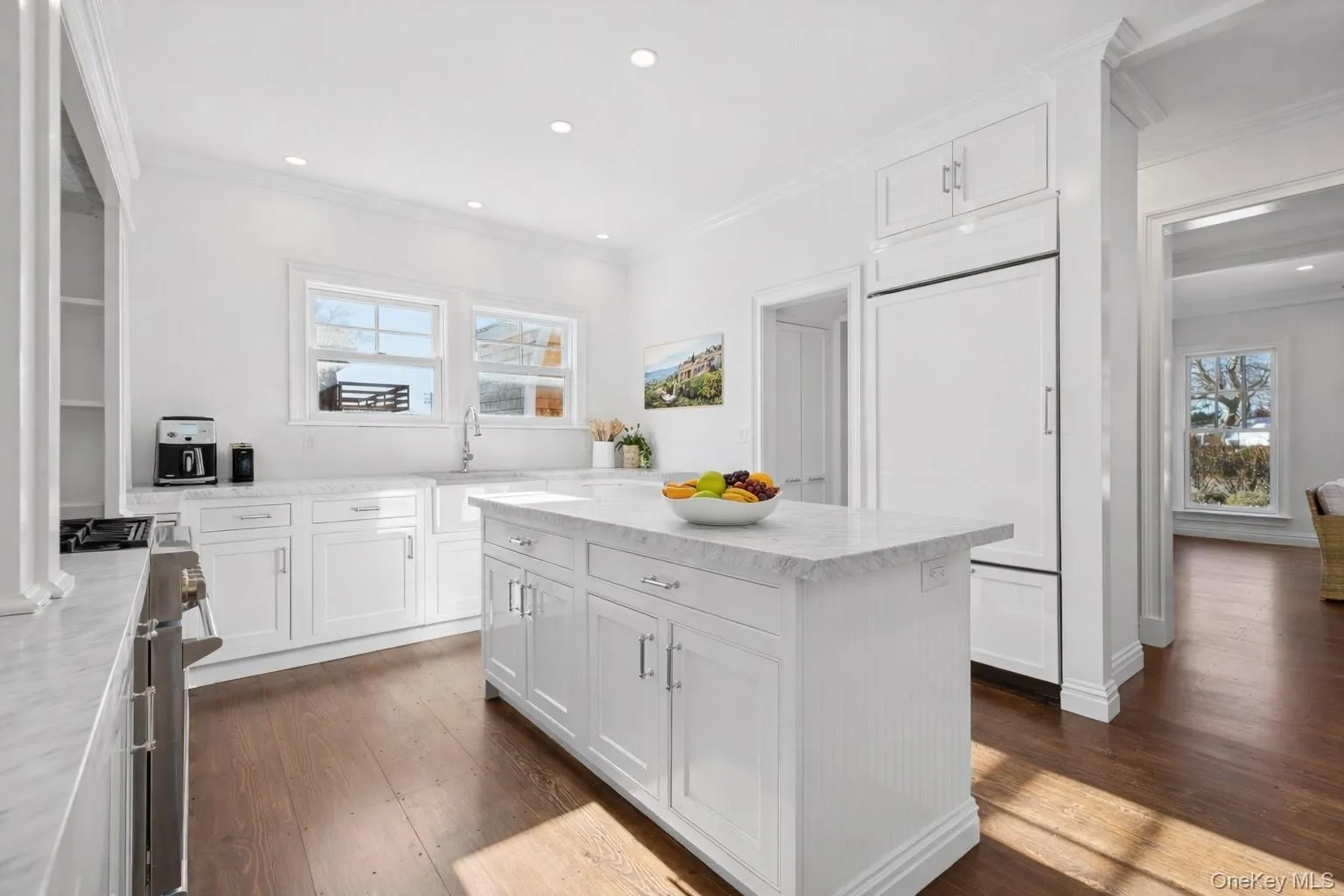 Kitchen featuring white cabinets, crown molding, dark wood-style floors, premium appliances, and light stone countertops Kitchen featuring white cabinets, crown molding, dark wood-style floors, premium appliances, and light stone countertops
