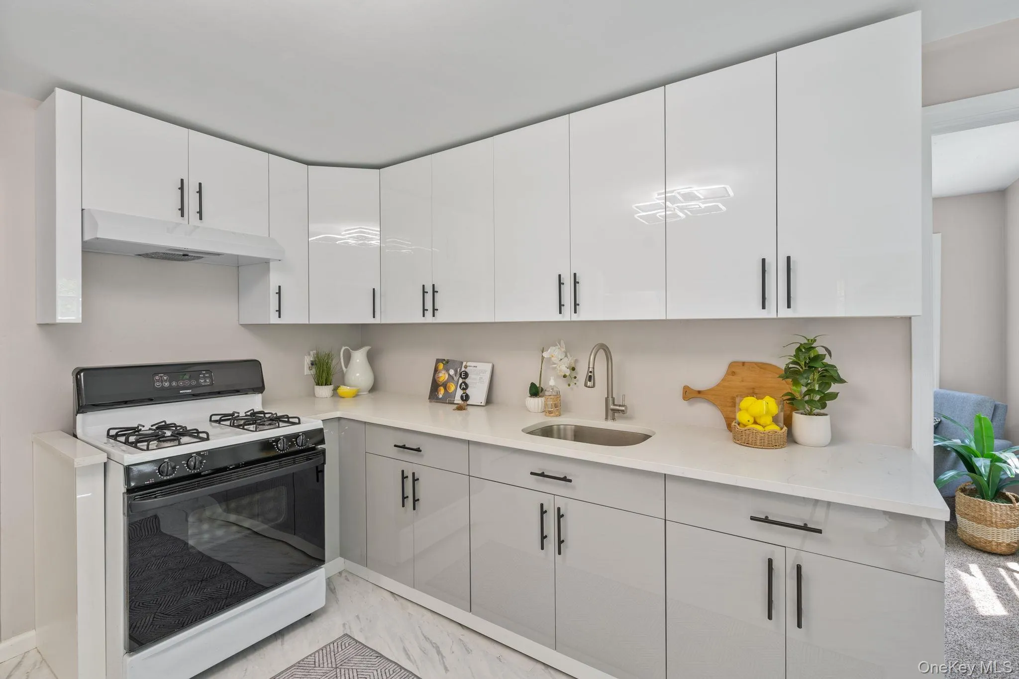 Kitchen featuring gas range, under cabinet range hood, light marble finish flooring, white cabinets, and light stone counters Kitchen featuring gas range, under cabinet range hood, light marble finish flooring, white cabinets, and light stone counters