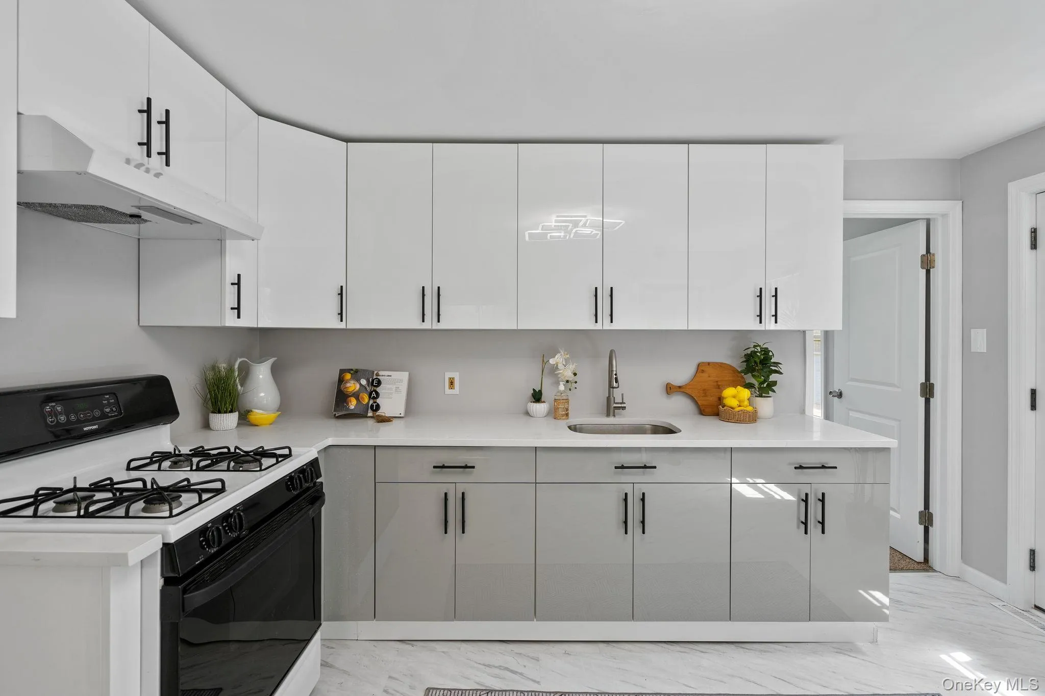 Kitchen with range with gas stovetop, under cabinet range hood, light marble finish floors, and white cabinetry Kitchen with range with gas stovetop, under cabinet range hood, light marble finish floors, and white cabinetry
