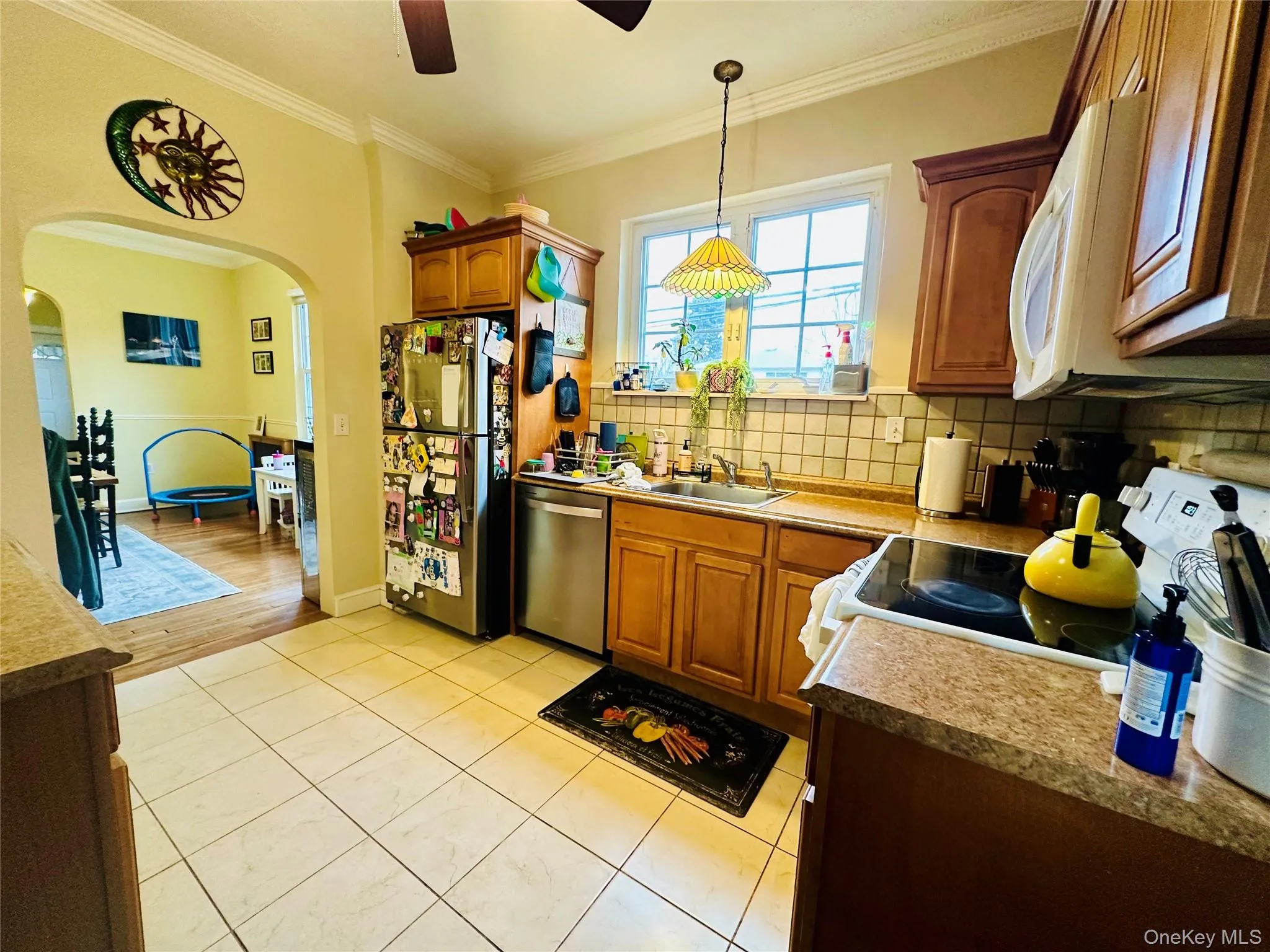 Kitchen featuring ornamental molding, stainless steel appliances, brown cabinets, and decorative light fixtures Kitchen featuring ornamental molding, stainless steel appliances, brown cabinets, and decorative light fixtures