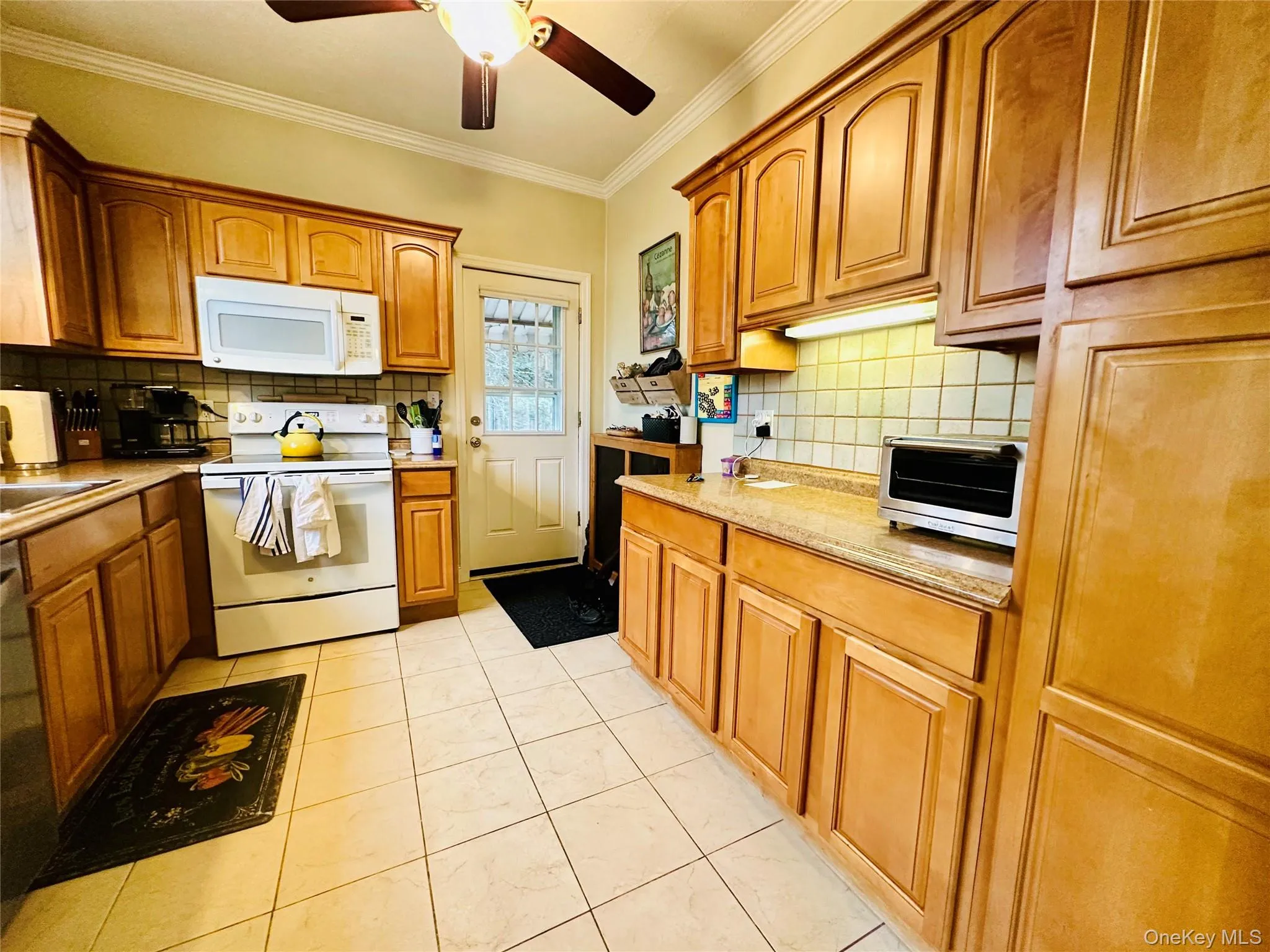 Kitchen with white appliances, ornamental molding, brown cabinets, a ceiling fan, and light stone counters Kitchen with white appliances, ornamental molding, brown cabinets, a ceiling fan, and light stone counters