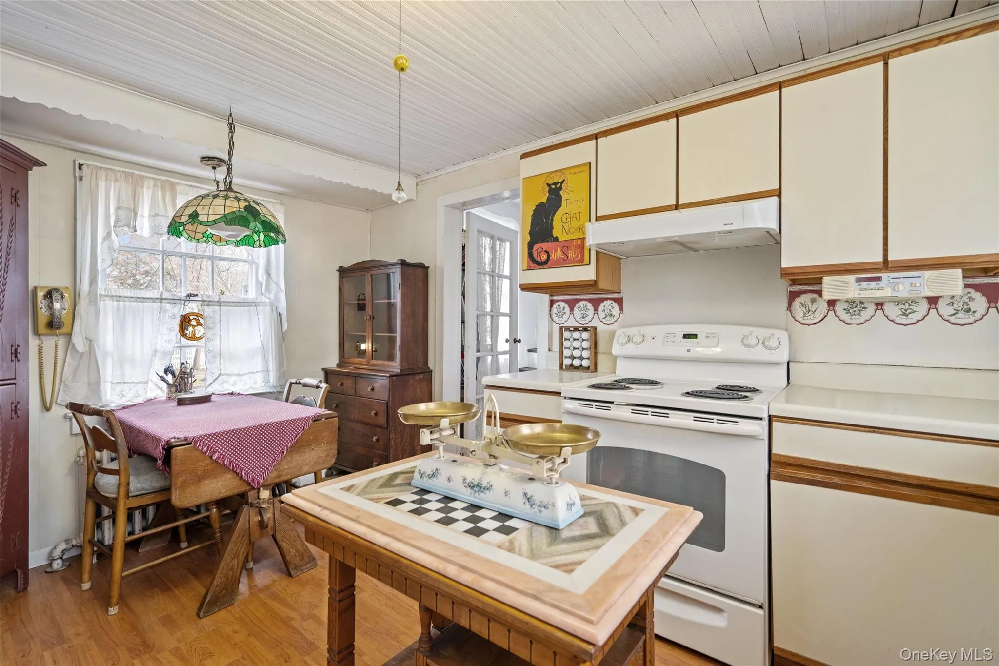 Kitchen with white range with electric cooktop, light countertops, under cabinet range hood, light wood-type flooring, and brown cabinets Kitchen with white range with electric cooktop, light countertops, under cabinet range hood, light wood-type flooring, and brown cabinets