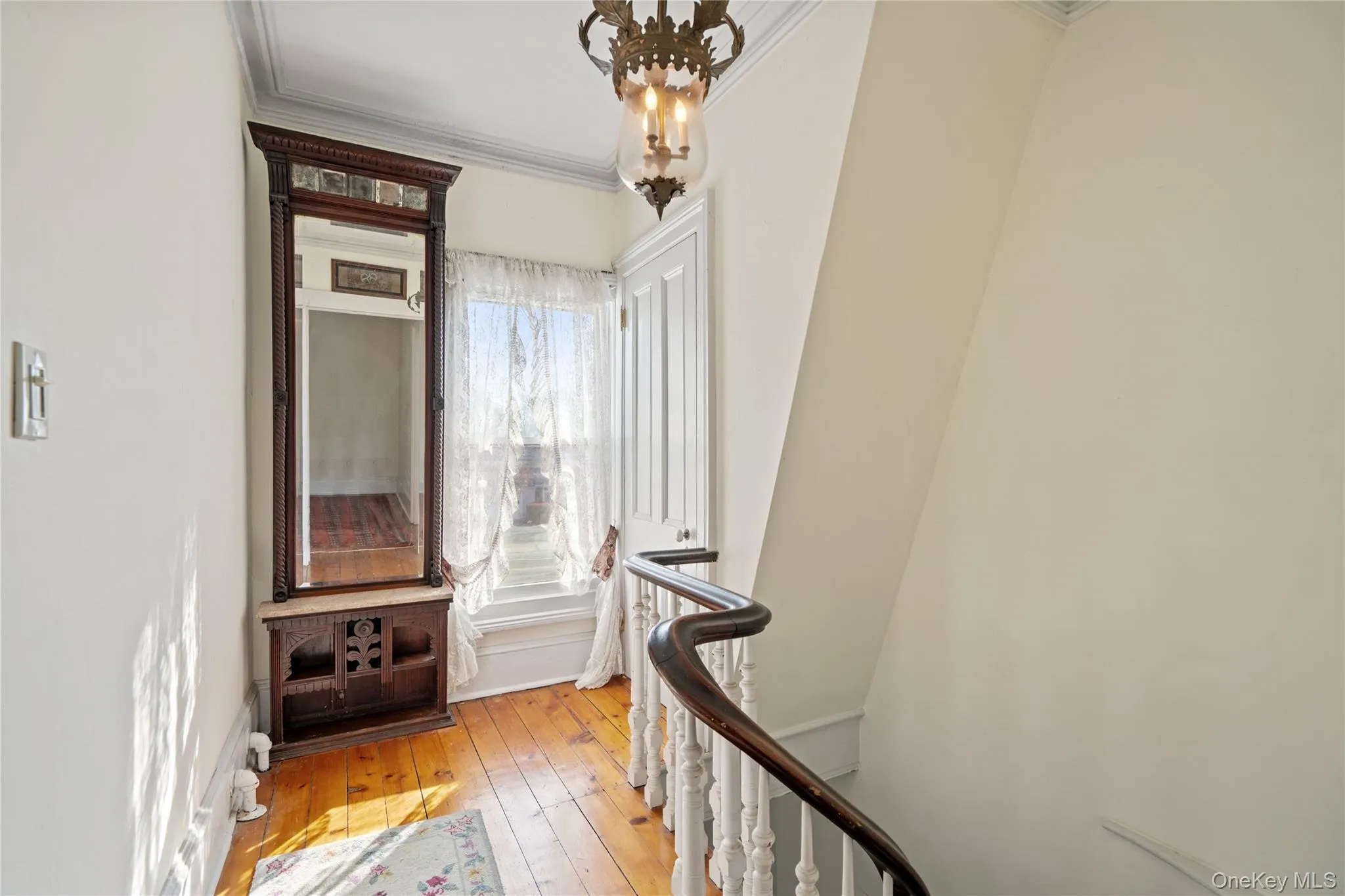 Hallway with light wood-style floors, ornamental molding, an upstairs landing, and a chandelier Hallway with light wood-style floors, ornamental molding, an upstairs landing, and a chandelier