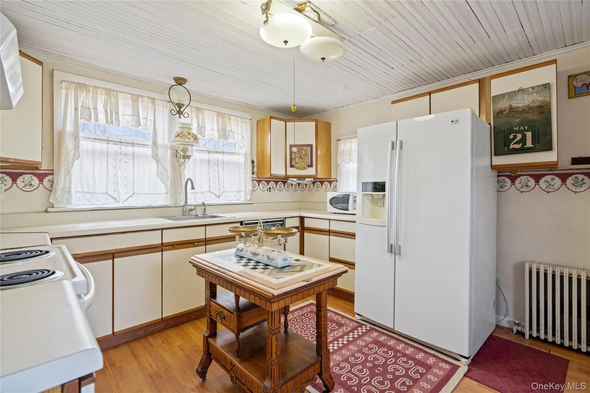 Kitchen with white appliances, light countertops, radiator, brown cabinetry, and light wood-style flooring Kitchen with white appliances, light countertops, radiator, brown cabinetry, and light wood-style flooring