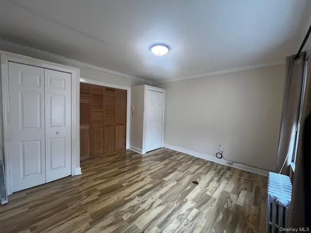 Unfurnished bedroom with wood finished floors, two closets, crown molding, and radiator Unfurnished bedroom with wood finished floors, two closets, crown molding, and radiator