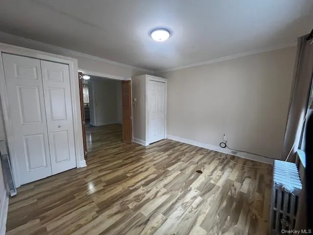Unfurnished bedroom featuring wood finished floors, radiator heating unit, and ornamental molding Unfurnished bedroom featuring wood finished floors, radiator heating unit, and ornamental molding