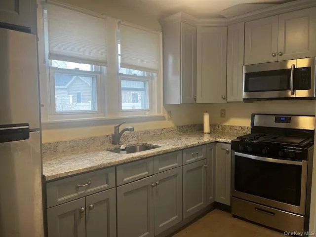 Kitchen with stainless steel appliances, light stone countertops, and gray cabinetry Kitchen with stainless steel appliances, light stone countertops, and gray cabinetry