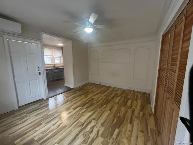 Unfurnished bedroom with a closet, light wood-style flooring, an AC wall unit, a ceiling fan, and ensuite bath Unfurnished bedroom with a closet, light wood-style flooring, an AC wall unit, a ceiling fan, and ensuite bath