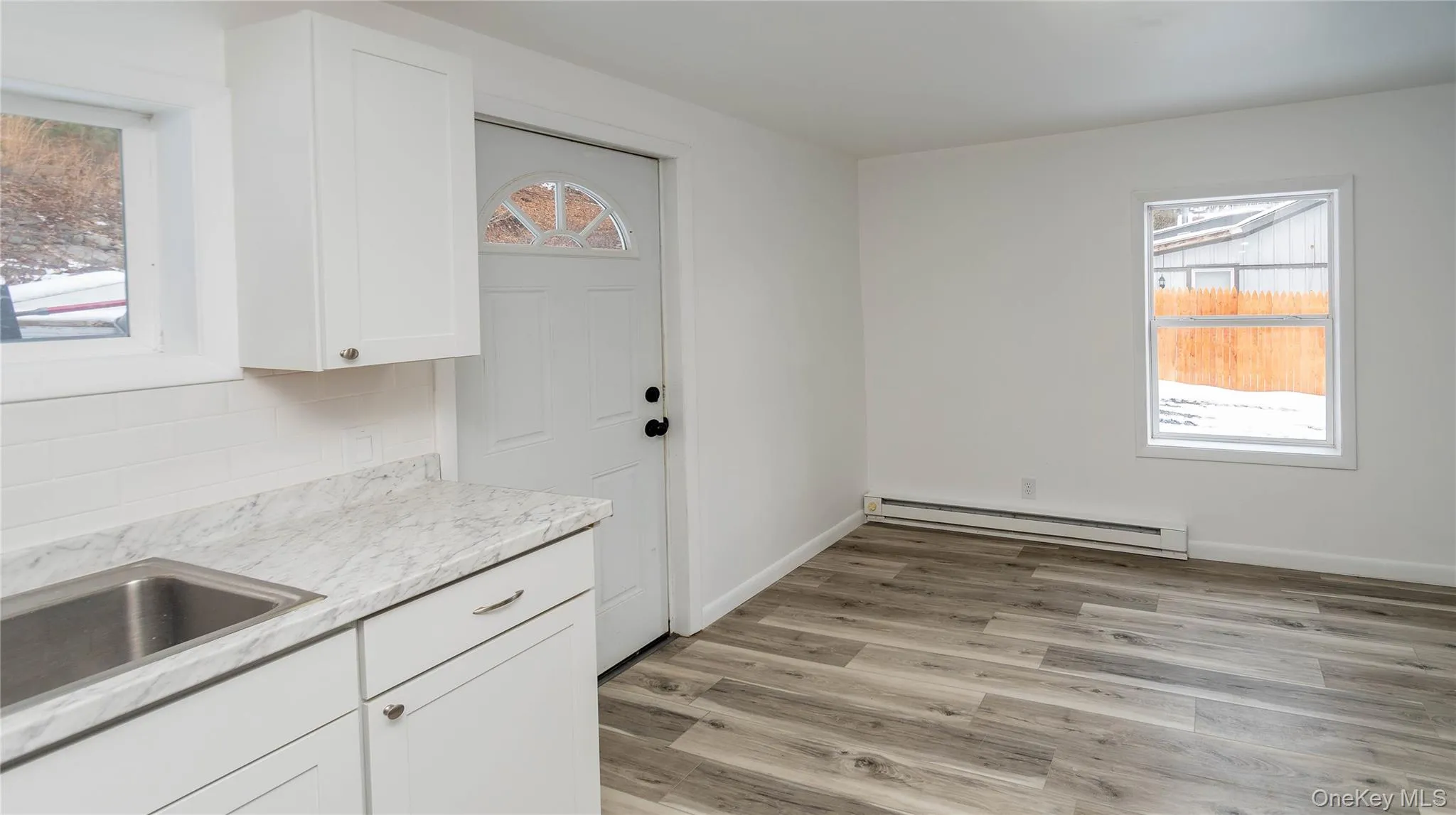 Kitchen with white cabinets, baseboard heating, light wood-style floors, and light stone countertops Kitchen with white cabinets, baseboard heating, light wood-style floors, and light stone countertops
