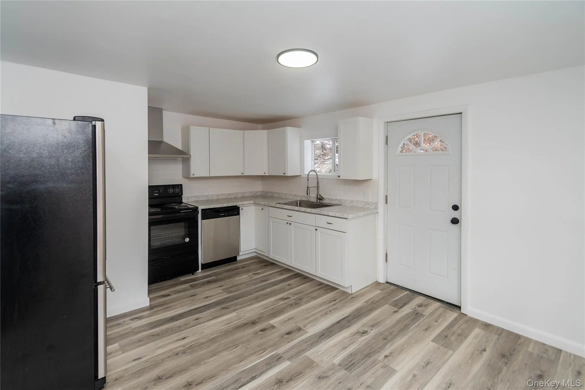 Kitchen featuring stainless steel appliances, light countertops, wall chimney exhaust hood, white cabinetry, and light wood-style flooring Kitchen featuring stainless steel appliances, light countertops, wall chimney exhaust hood, white cabinetry, and light wood-style flooring