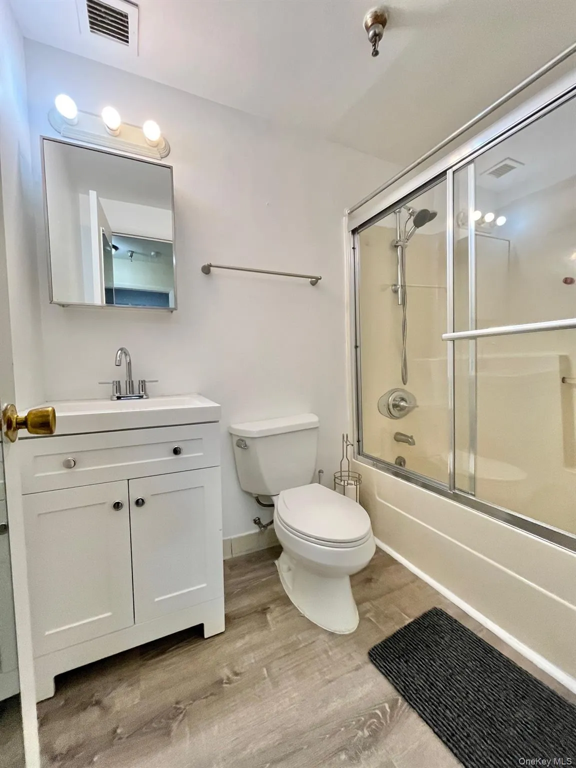 Full bathroom with enclosed tub / shower combo, vanity, and light wood finished floors. Full bathroom with enclosed tub / shower combo, vanity, and light wood finished floors.