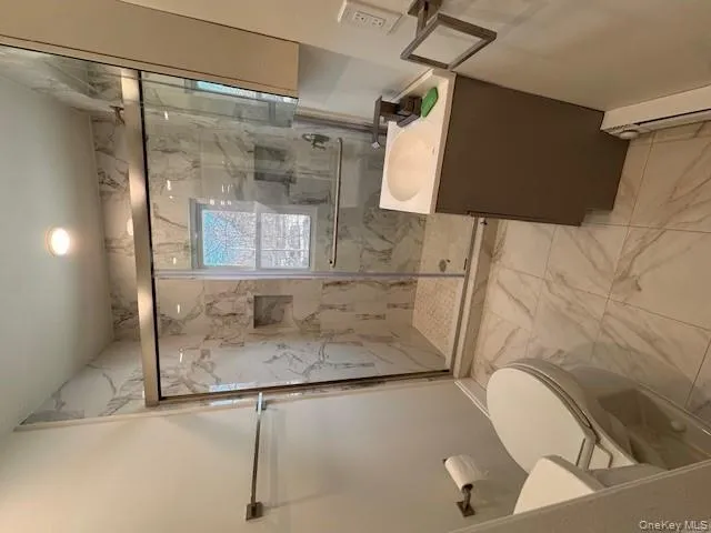 Full bath with light marble finish flooring, vanity, a marble finish shower, and baseboard heating Full bath with light marble finish flooring, vanity, a marble finish shower, and baseboard heating