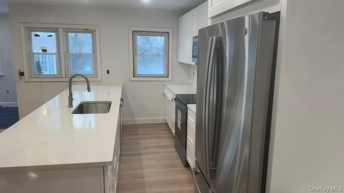 Kitchen with freestanding refrigerator, a peninsula, white cabinetry, black range with electric stovetop, and dark wood finished floors Kitchen with freestanding refrigerator, a peninsula, white cabinetry, black range with electric stovetop, and dark wood finished floors