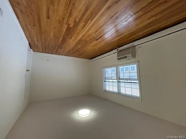 Spare room with light wood-style flooring, baseboard heating, and an AC wall unit Spare room with light wood-style flooring, baseboard heating, and an AC wall unit
