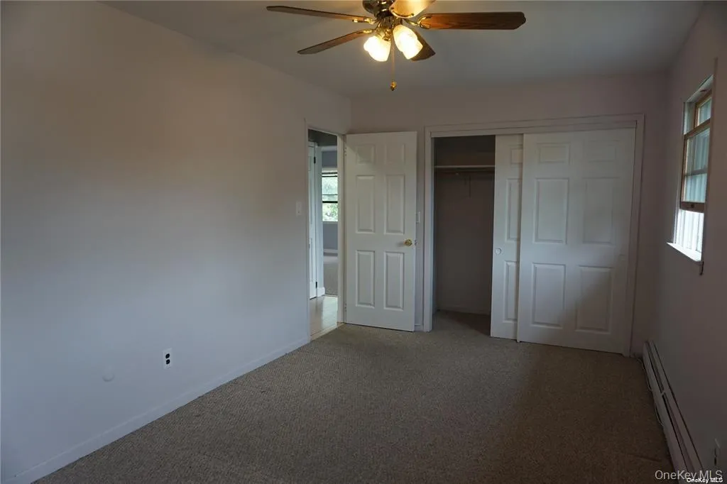 Unfurnished bedroom with baseboard heating, carpet floors, a closet, and a ceiling fan Unfurnished bedroom with baseboard heating, carpet floors, a closet, and a ceiling fan