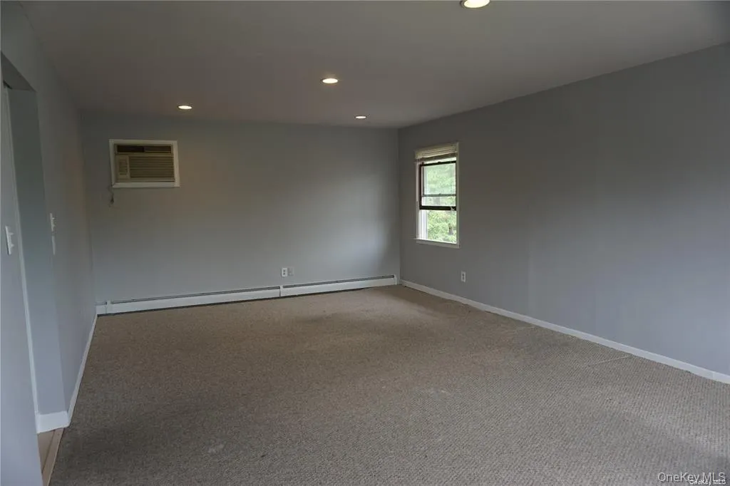 Carpeted empty room with recessed lighting, a baseboard radiator, and a wall mounted air conditioner Carpeted empty room with recessed lighting, a baseboard radiator, and a wall mounted air conditioner