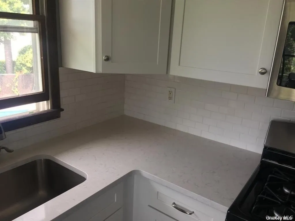 Kitchen featuring black range with gas stovetop, stainless steel microwave, white cabinetry, light stone counters, and decorative backsplash Kitchen featuring black range with gas stovetop, stainless steel microwave, white cabinetry, light stone counters, and decorative backsplash