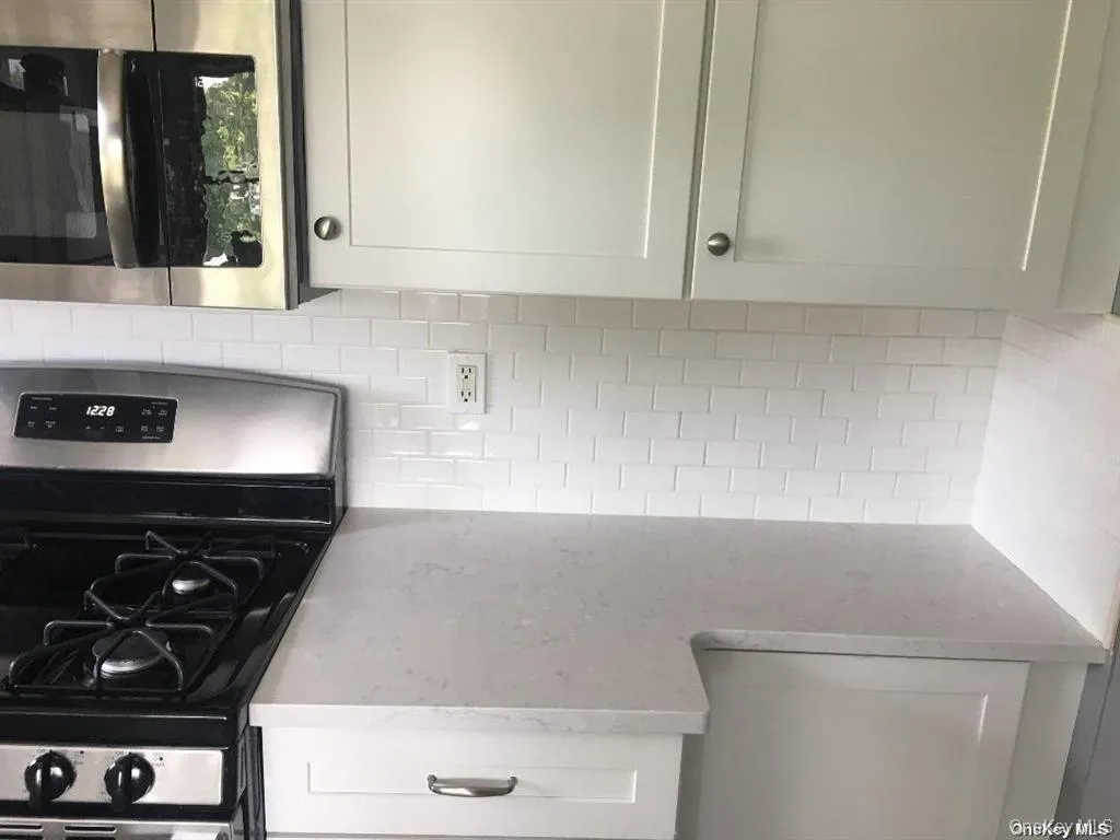 Kitchen featuring appliances with stainless steel finishes, light stone counters, white cabinetry, and backsplash Kitchen featuring appliances with stainless steel finishes, light stone counters, white cabinetry, and backsplash