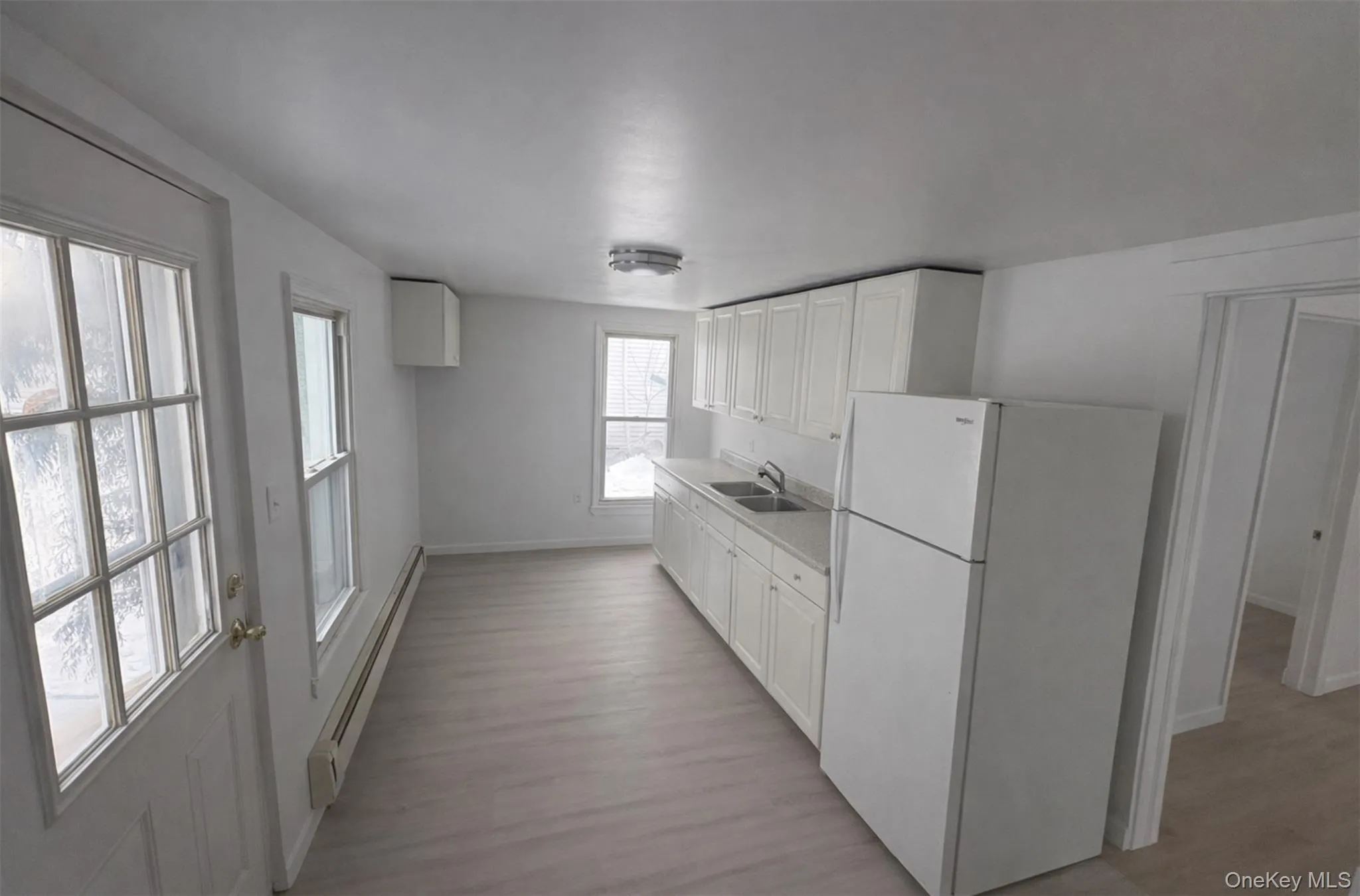 Kitchen featuring freestanding refrigerator, light countertops, baseboard heating, white cabinets, and light wood-style floors Kitchen featuring freestanding refrigerator, light countertops, baseboard heating, white cabinets, and light wood-style floors