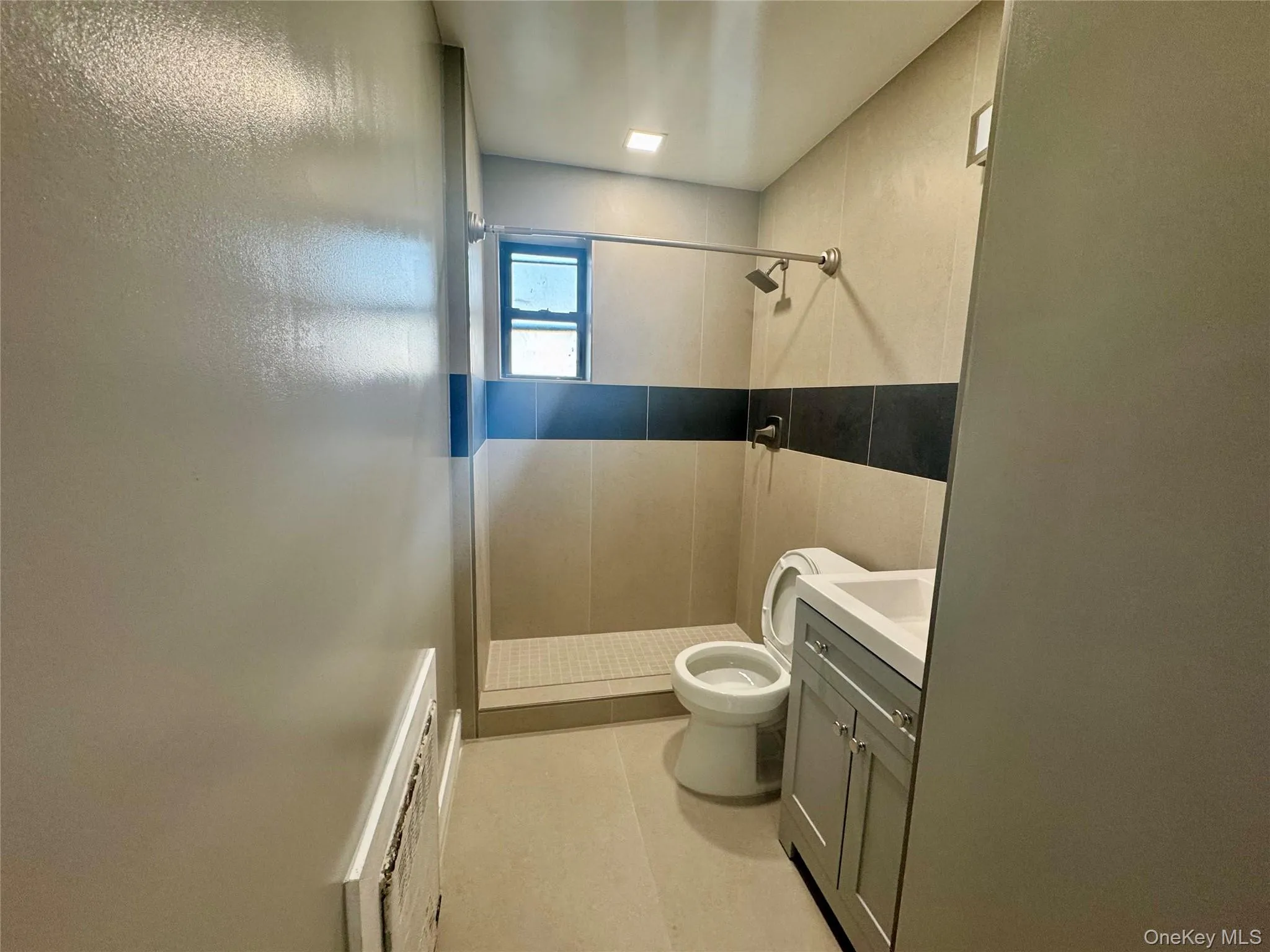 Bathroom featuring a tile shower, tile patterned flooring, toilet, vanity, and tile walls Bathroom featuring a tile shower, tile patterned flooring, toilet, vanity, and tile walls