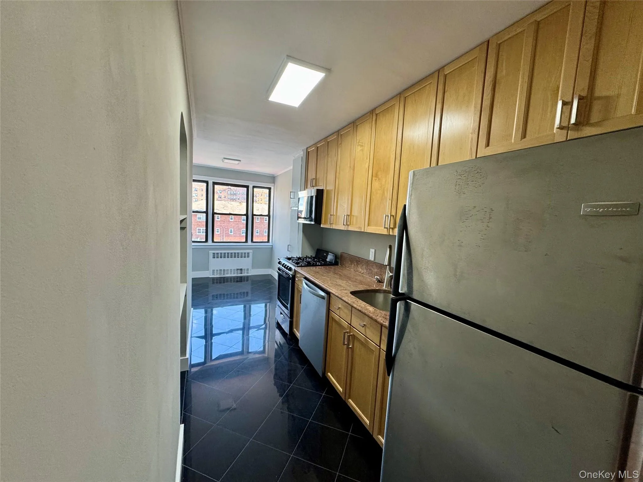 Kitchen with appliances with stainless steel finishes, light brown cabinets, dark tile patterned flooring, and radiator Kitchen with appliances with stainless steel finishes, light brown cabinets, dark tile patterned flooring, and radiator