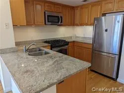 Kitchen featuring brown cabinetry, appliances with stainless steel finishes, a peninsula, light wood-style flooring, and light stone counters Kitchen featuring brown cabinetry, appliances with stainless steel finishes, a peninsula, light wood-style flooring, and light stone counters