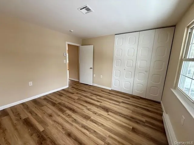 Unfurnished bedroom with New wood finished floors, a closet, and baseboard heating Unfurnished bedroom with New wood finished floors, a closet, and baseboard heating