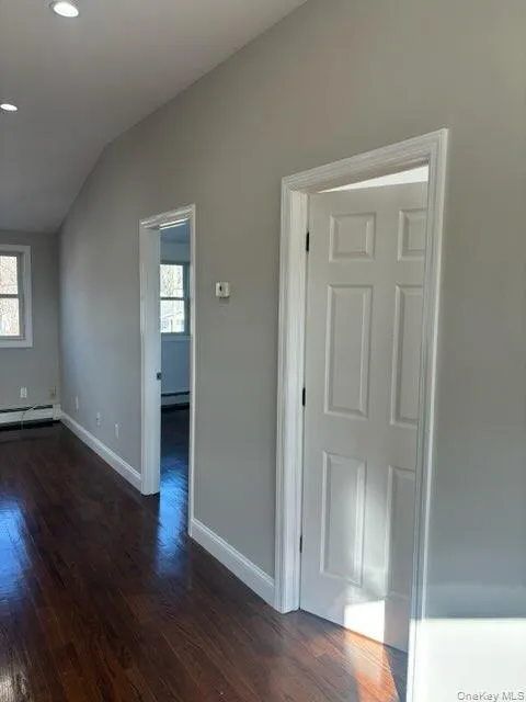 Empty room with dark wood finished floors, vaulted ceiling, recessed lighting, and baseboard heating Empty room with dark wood finished floors, vaulted ceiling, recessed lighting, and baseboard heating