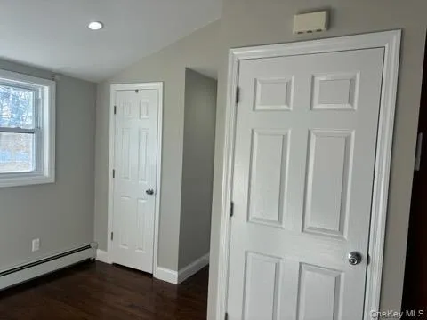 Unfurnished bedroom featuring dark wood-type flooring, lofted ceiling, and a baseboard heating unit Unfurnished bedroom featuring dark wood-type flooring, lofted ceiling, and a baseboard heating unit
