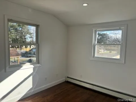 Unfurnished room with a baseboard heating unit, lofted ceiling, dark wood finished floors, and recessed lighting Unfurnished room with a baseboard heating unit, lofted ceiling, dark wood finished floors, and recessed lighting