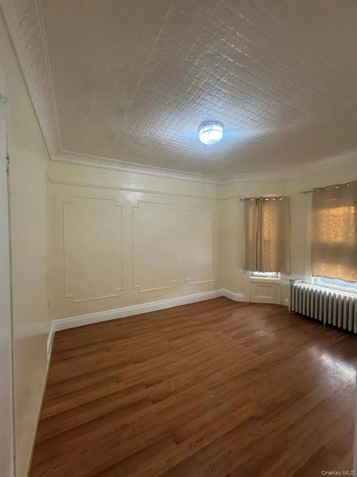 Empty room featuring a decorative wall, dark wood-style floors, radiator heating unit, and crown molding Empty room featuring a decorative wall, dark wood-style floors, radiator heating unit, and crown molding