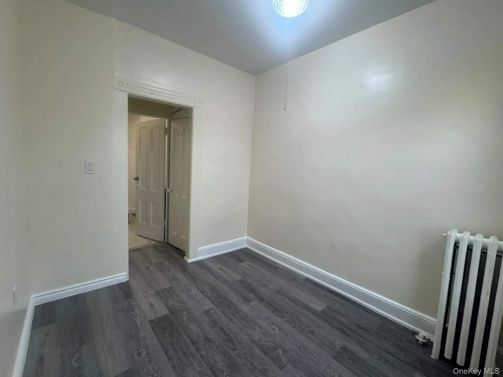 Spare room with radiator and dark wood-style floors Spare room with radiator and dark wood-style floors
